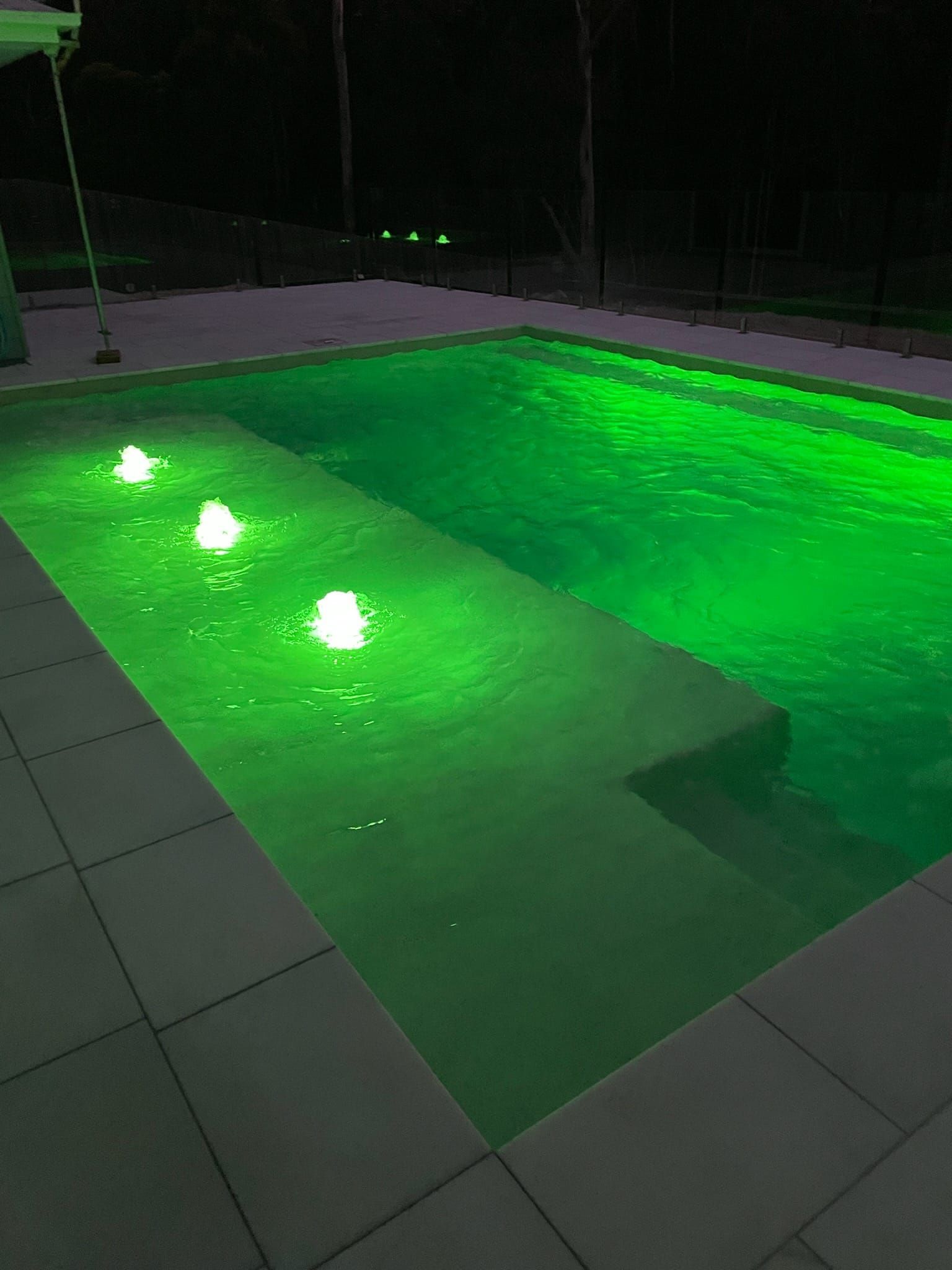 A Large Swimming Pool Is Lit Up At Night With Green Lights — CJB Pools in Veteran, QLD