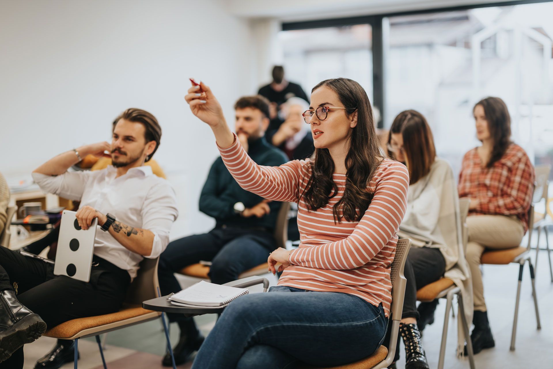 People seated in a classroom, one woman raising her hand during a discussion