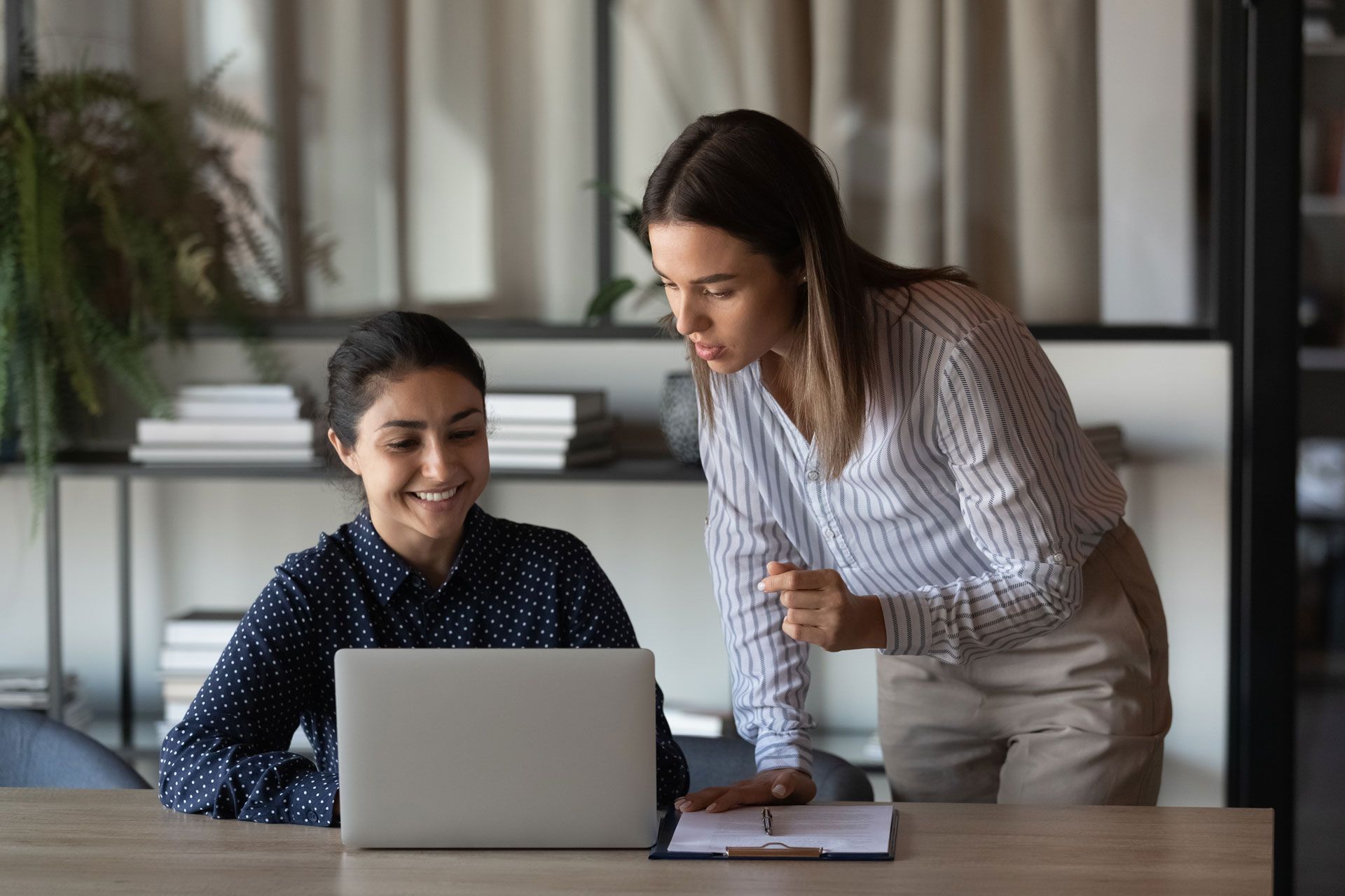 An adult and a child sitting at a desk, the adult pointing at the child's paper.