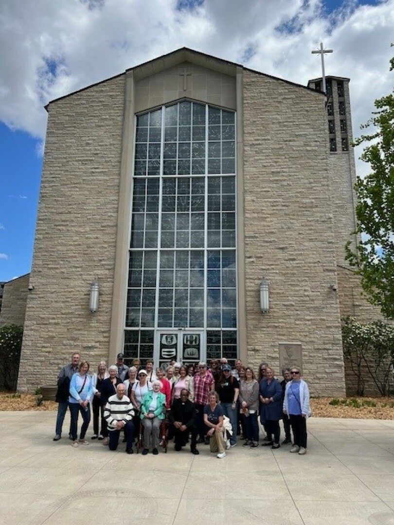 A group of people poses in front of a large church with a stone facade and tall glass windows.