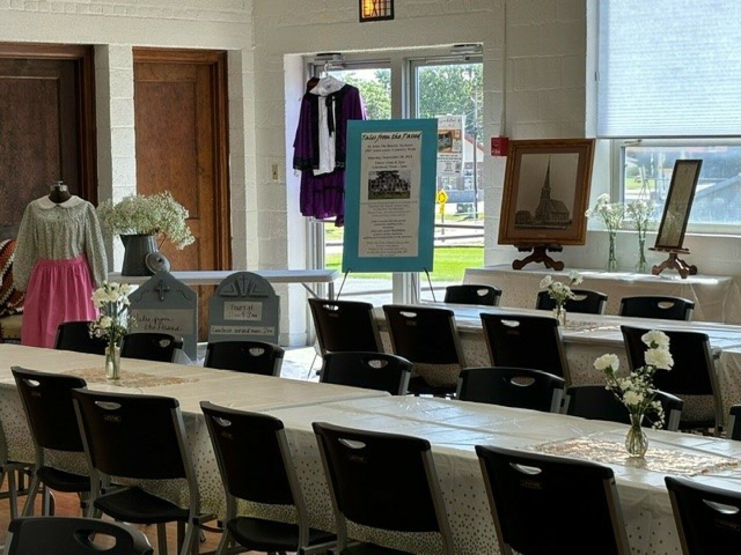 A room set for an event with long tables covered in white tablecloths and adorned with small flower vases.