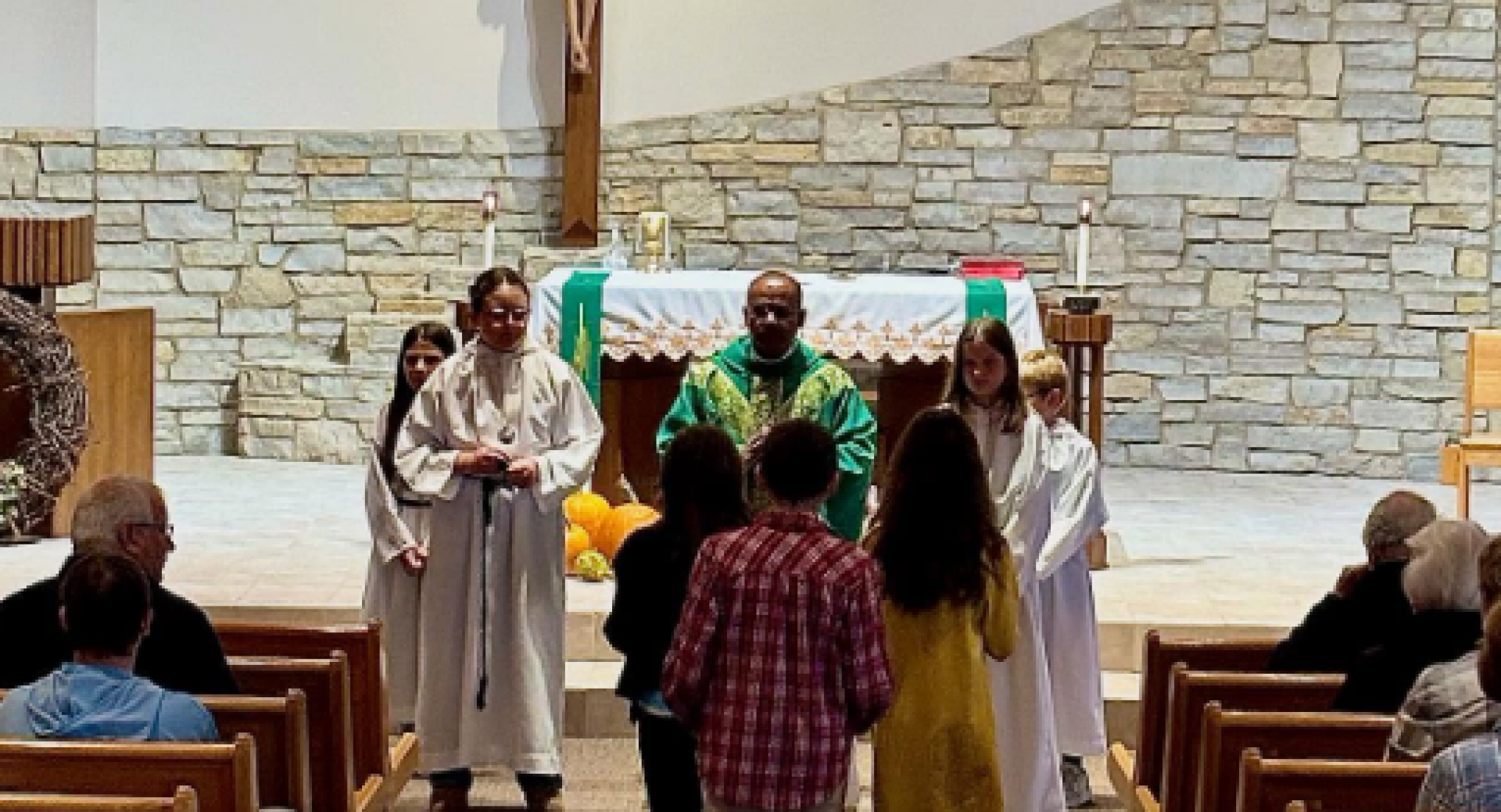 A priest in green robes stands at the altar of a stone-walled church. 