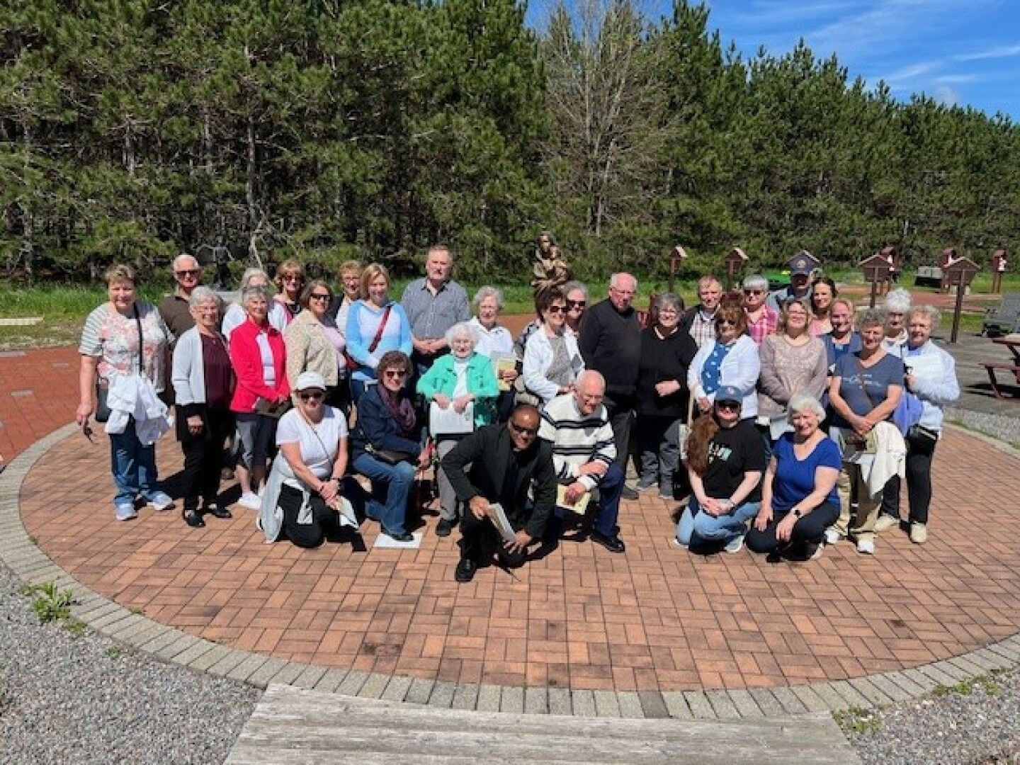 A group of about thirty people, mostly older adults, pose together outdoors on a sunny day.
