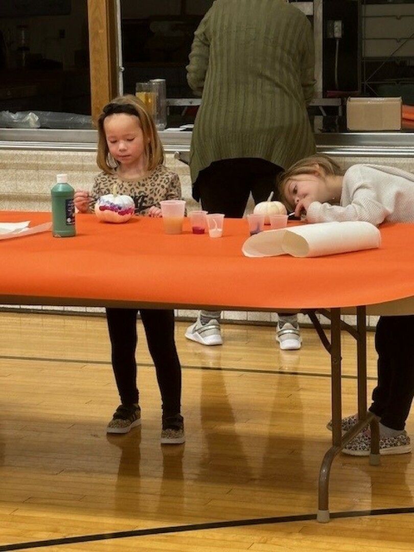 Two young children engage in arts and crafts at an orange-covered table.