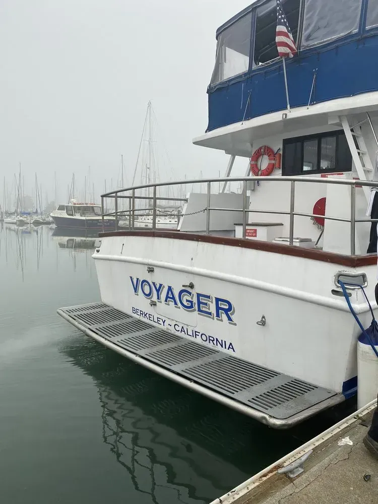 White Voyager boat docked in water; California, USA. Blue accents, cloudy day. White Voyager boat docked in water; California, USA. Blue accents, cloudy day.