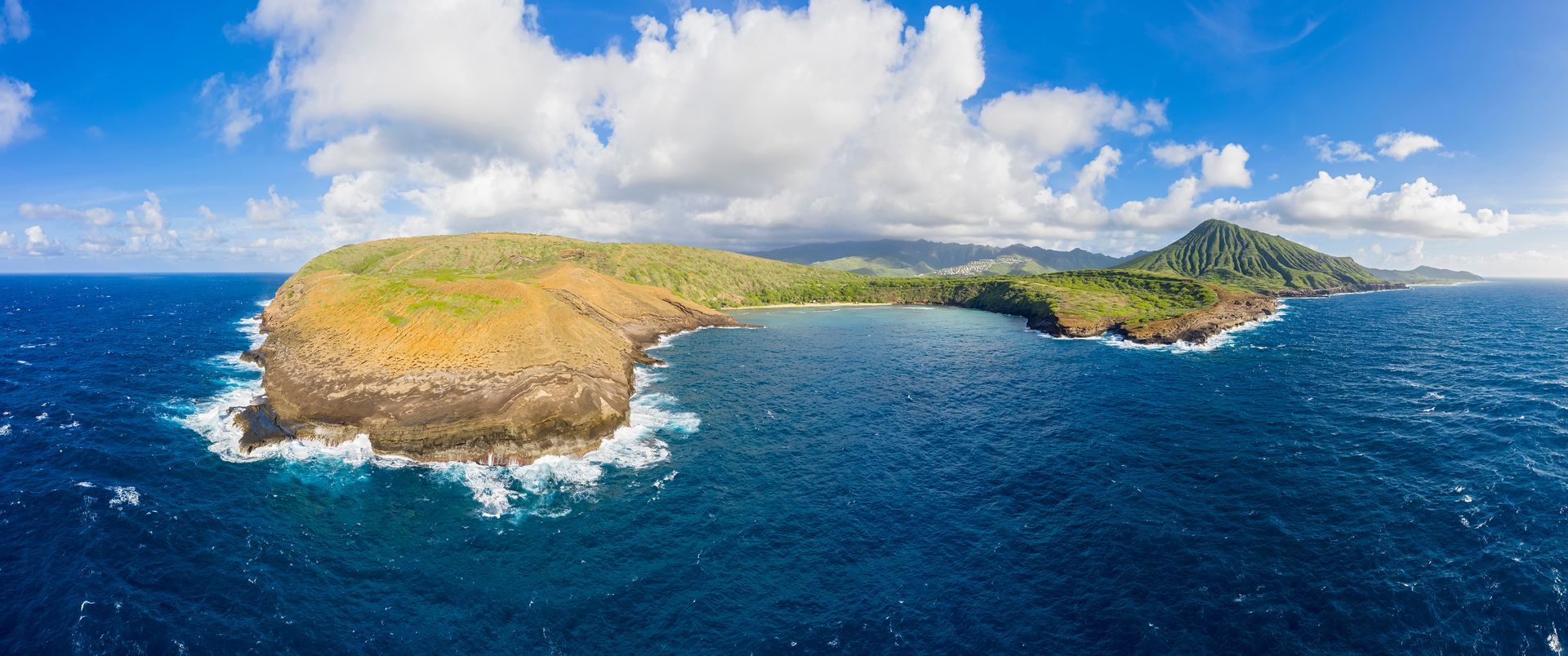 Panoramic view of a rocky island surrounded by deep blue ocean under a bright blue sky with puffy clouds. Panoramic view of a rocky island surrounded by deep blue ocean under a bright blue sky with puffy clouds.