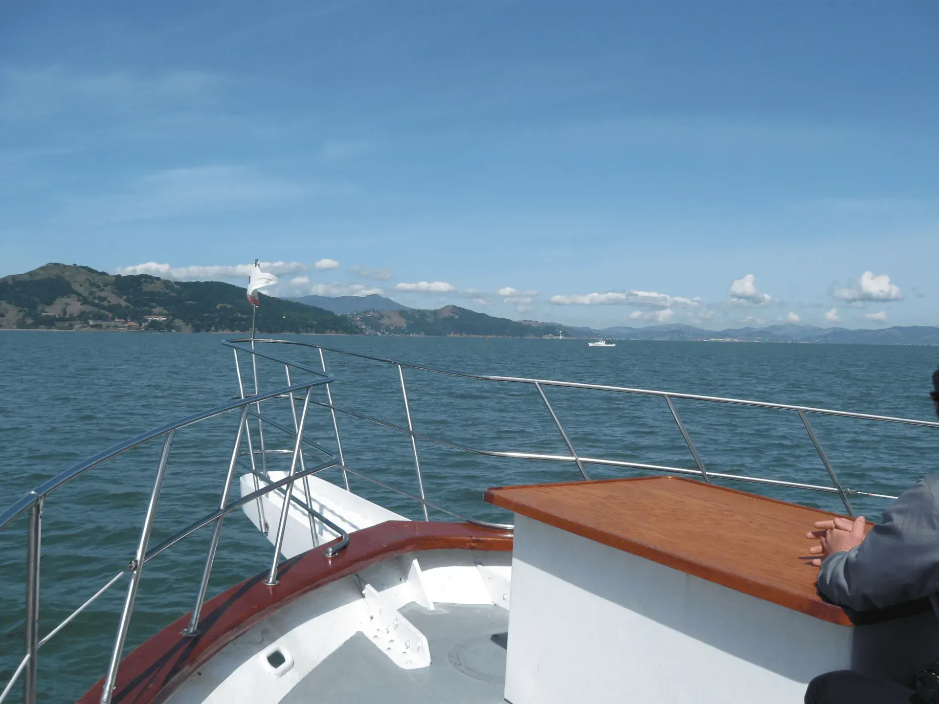 Boat sailing on water with land in background. Blue sky, sunny.