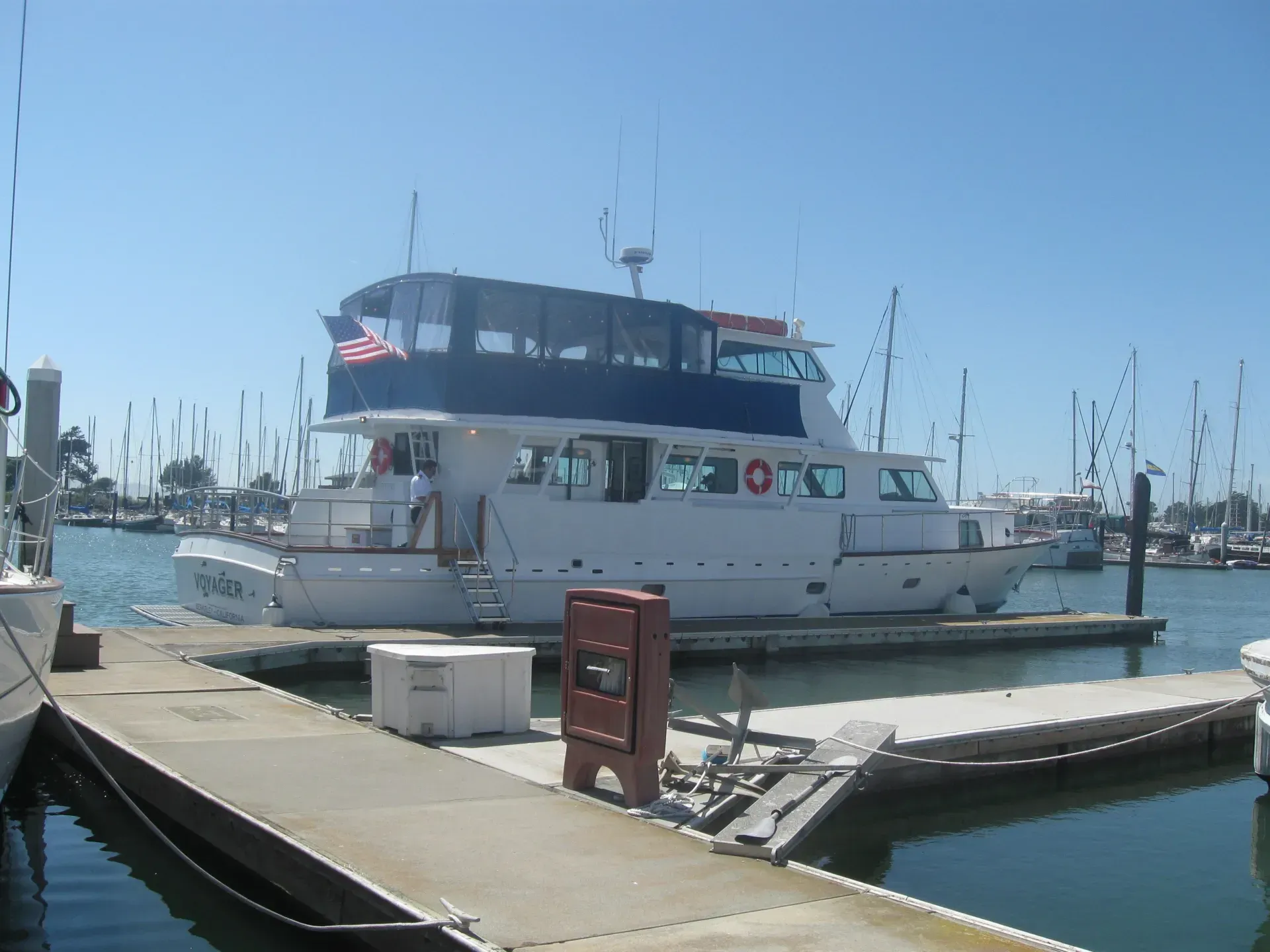 White boat docked at a marina with a blue awning and American flag, sunny day.