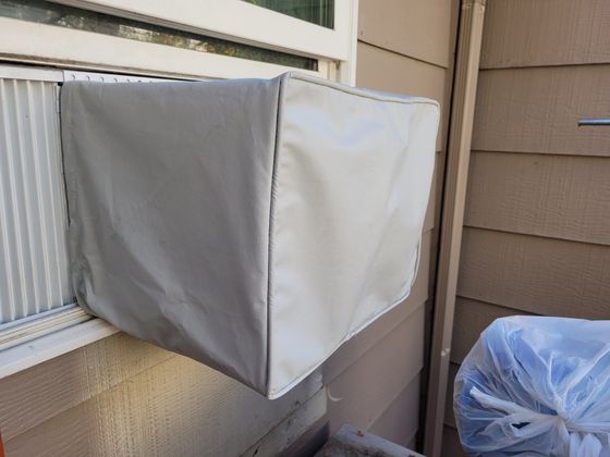 A window air conditioner is covered with a white cover.