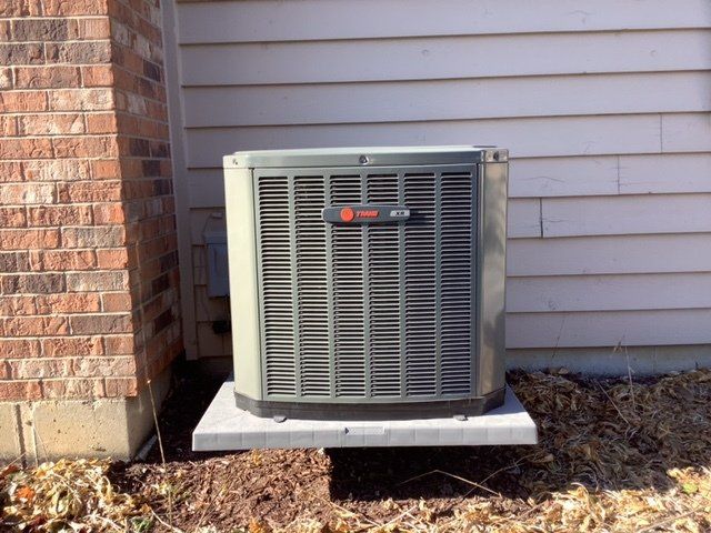 A trident air conditioner is sitting outside of a brick house