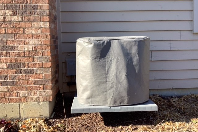 An air conditioner is sitting outside of a brick house