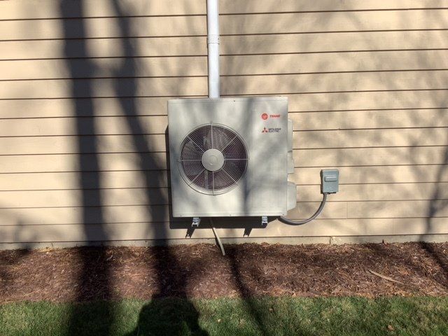 A white air conditioner is mounted on the side of a house.