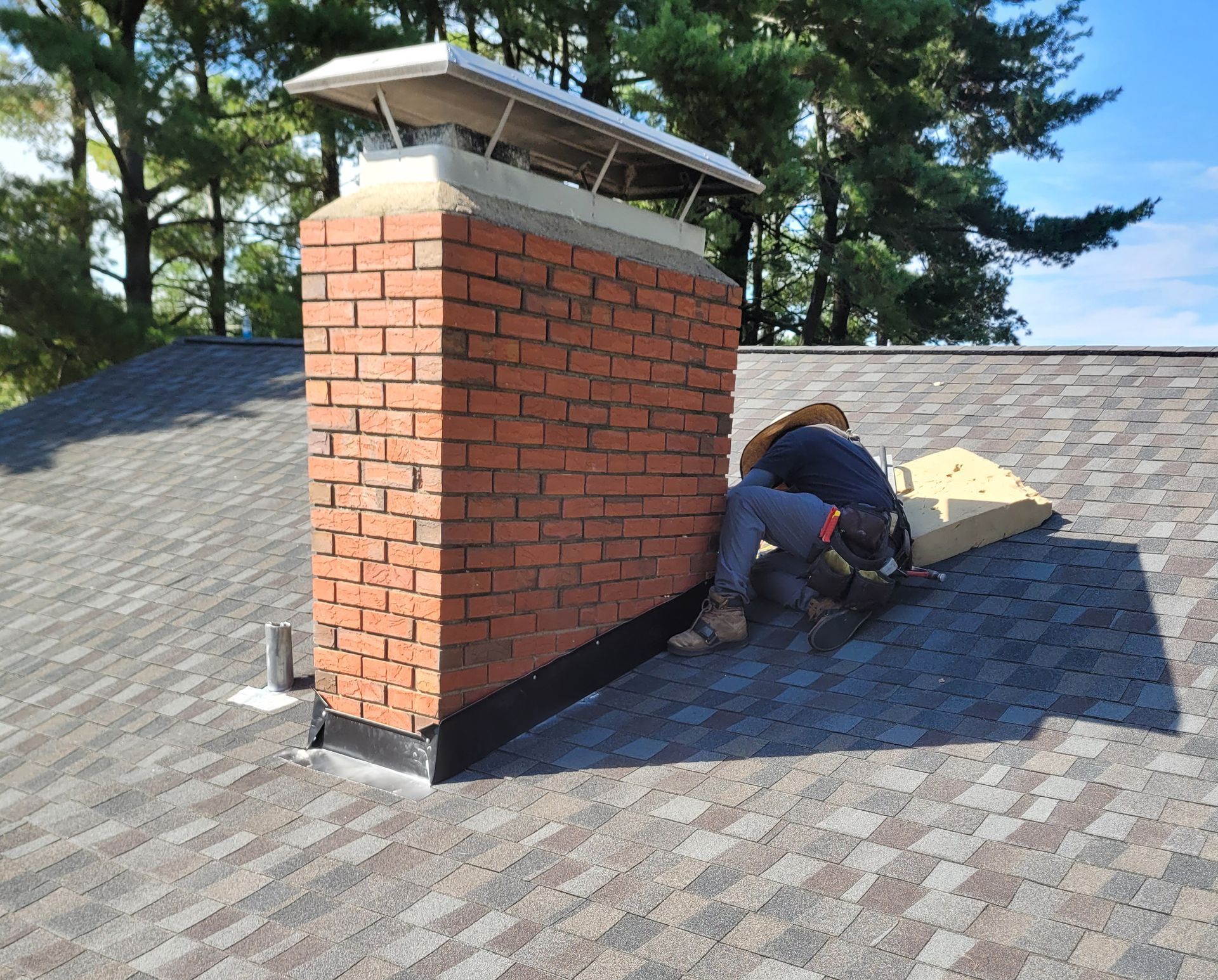 A man is working on a brick chimney on top of a roof.