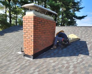 A man is working on a brick chimney on top of a roof.