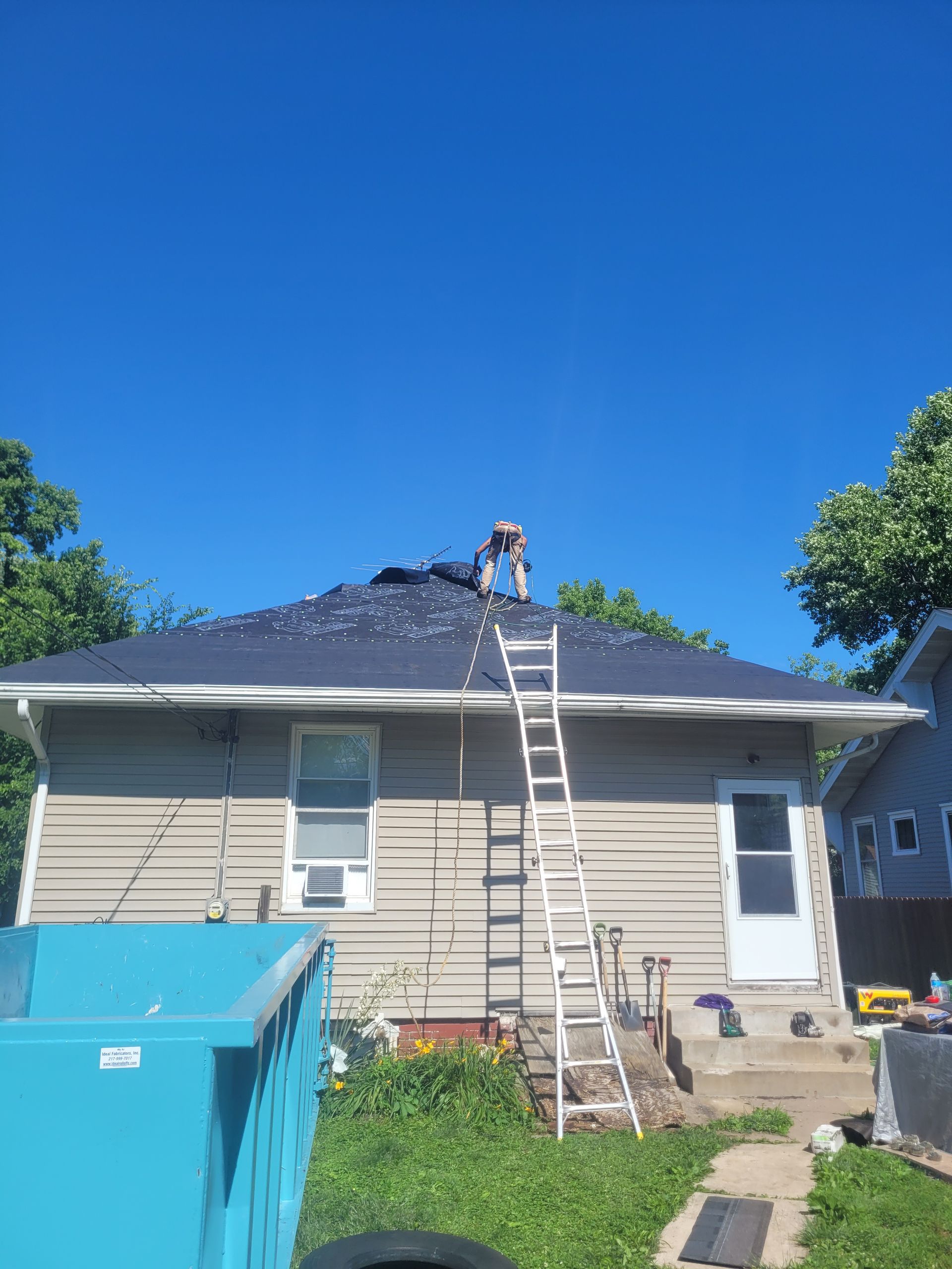 A man is standing on a ladder on the roof of a house.