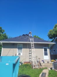 A man is standing on a ladder on the roof of a house.