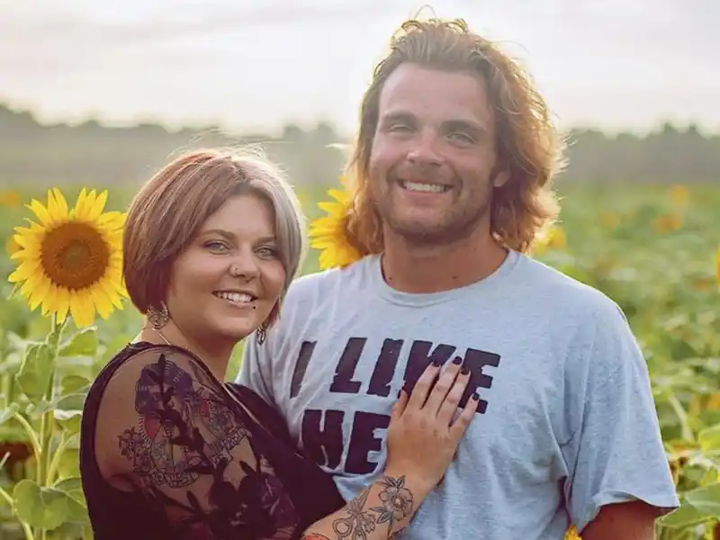 A man and a woman are posing for a picture in a field of sunflowers.