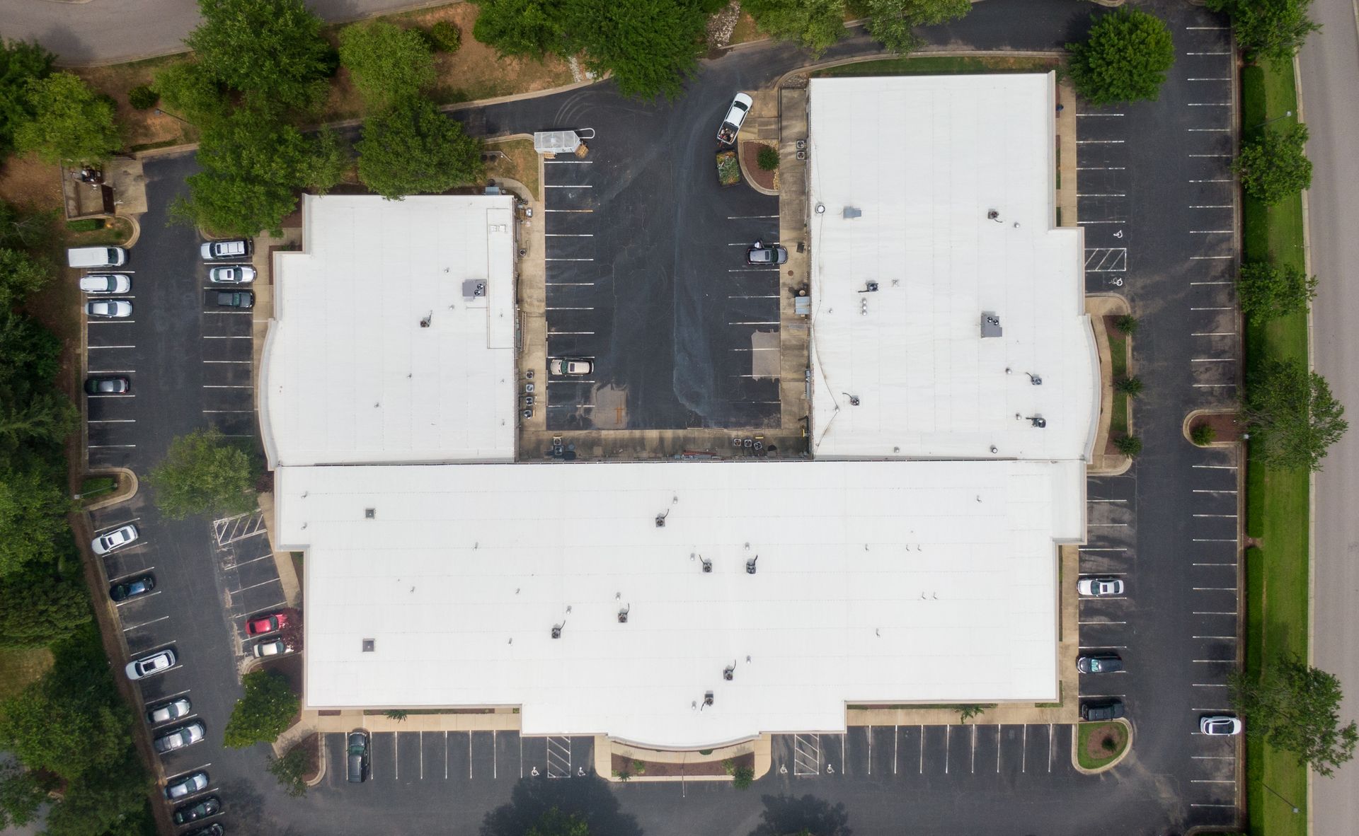 Aerial view of a white-roofed commercial building with surrounding parking lots and trees.