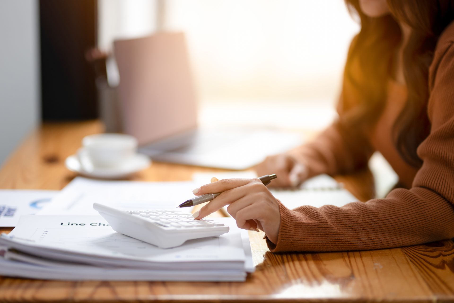 Person writing on a desk with a calculator and paperwork in warm sunlight