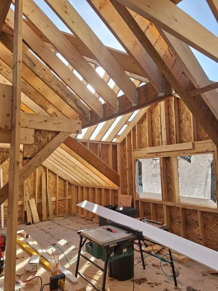 Unfinished attic with exposed wooden framing, roof windows, and a workbench under construction