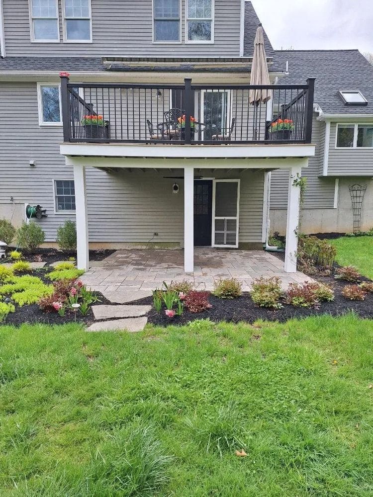 Backyard view of a house with a raised deck, covered patio, stone path, and landscaped garden beds