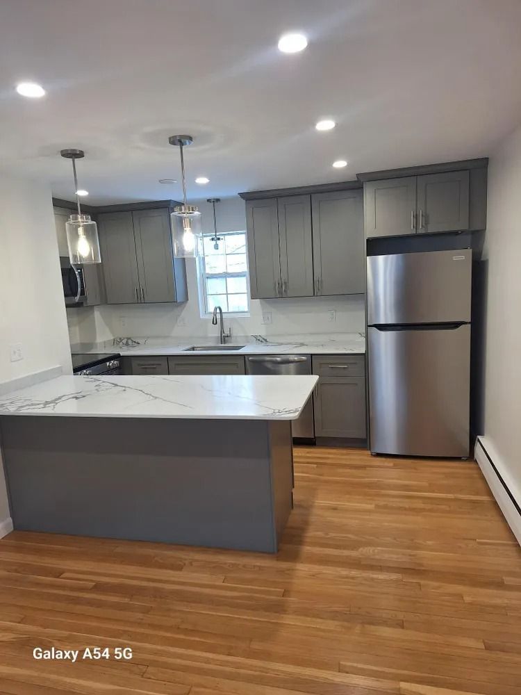 Modern kitchen with gray cabinets, stainless steel fridge, white island, and hardwood floors
