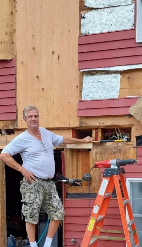 Man standing by a ladder beside a house with damaged siding and exposed insulation.