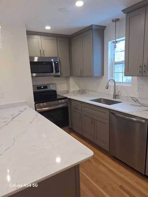 Modern kitchen with white marble countertops, gray cabinets, stainless appliances, and hardwood floors.