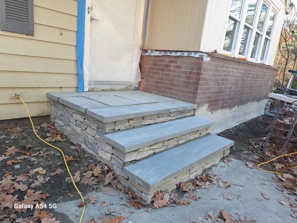 Front porch with new gray steps and landing under construction beside a tan house.