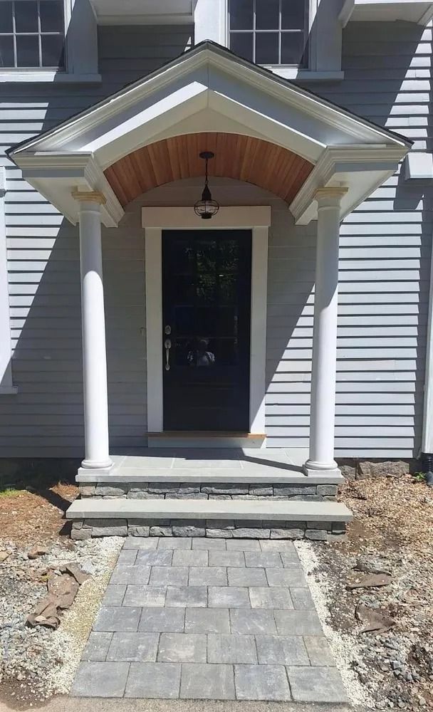 Front entrance of a gray house with white columns, covered porch, and stone walkway leading to the door