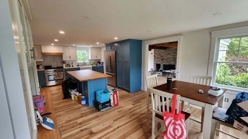 Open kitchen and dining area with wood floors, blue accent wall, and a table by a window.