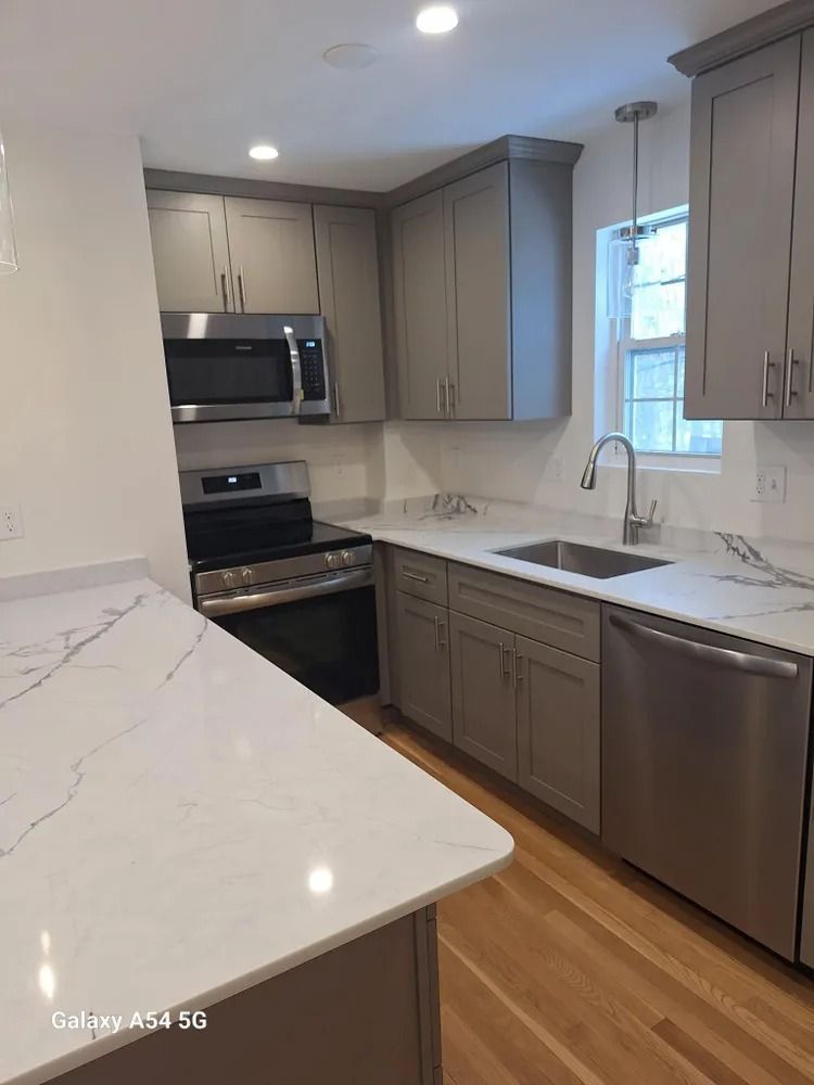 Modern kitchen with gray cabinets, white quartz countertops, stainless steel appliances, and a window over the sink