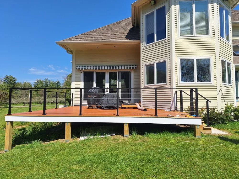 Backyard deck with black railing and patio furniture beside a tan two-story house
