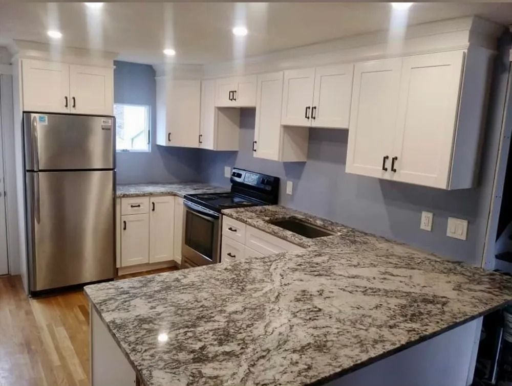 Modern kitchen with white cabinets, stainless steel fridge, and granite countertops, seen from the island.