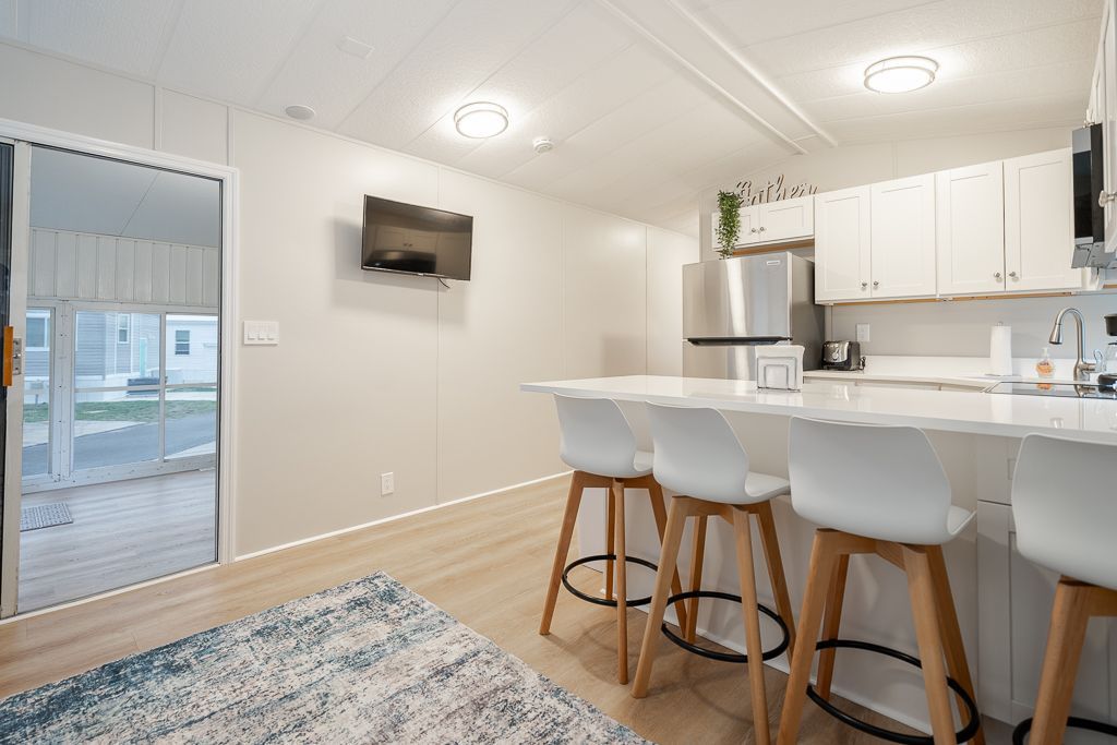 A modern kitchen with white cabinets, stainless steel appliances, and a marble-topped island with four white bar stools.