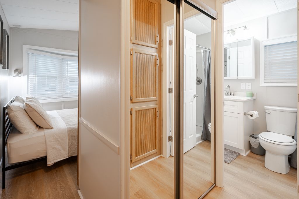 A bedroom with a bed beside a wooden wardrobe and a view into a bathroom with a white vanity and toilet.