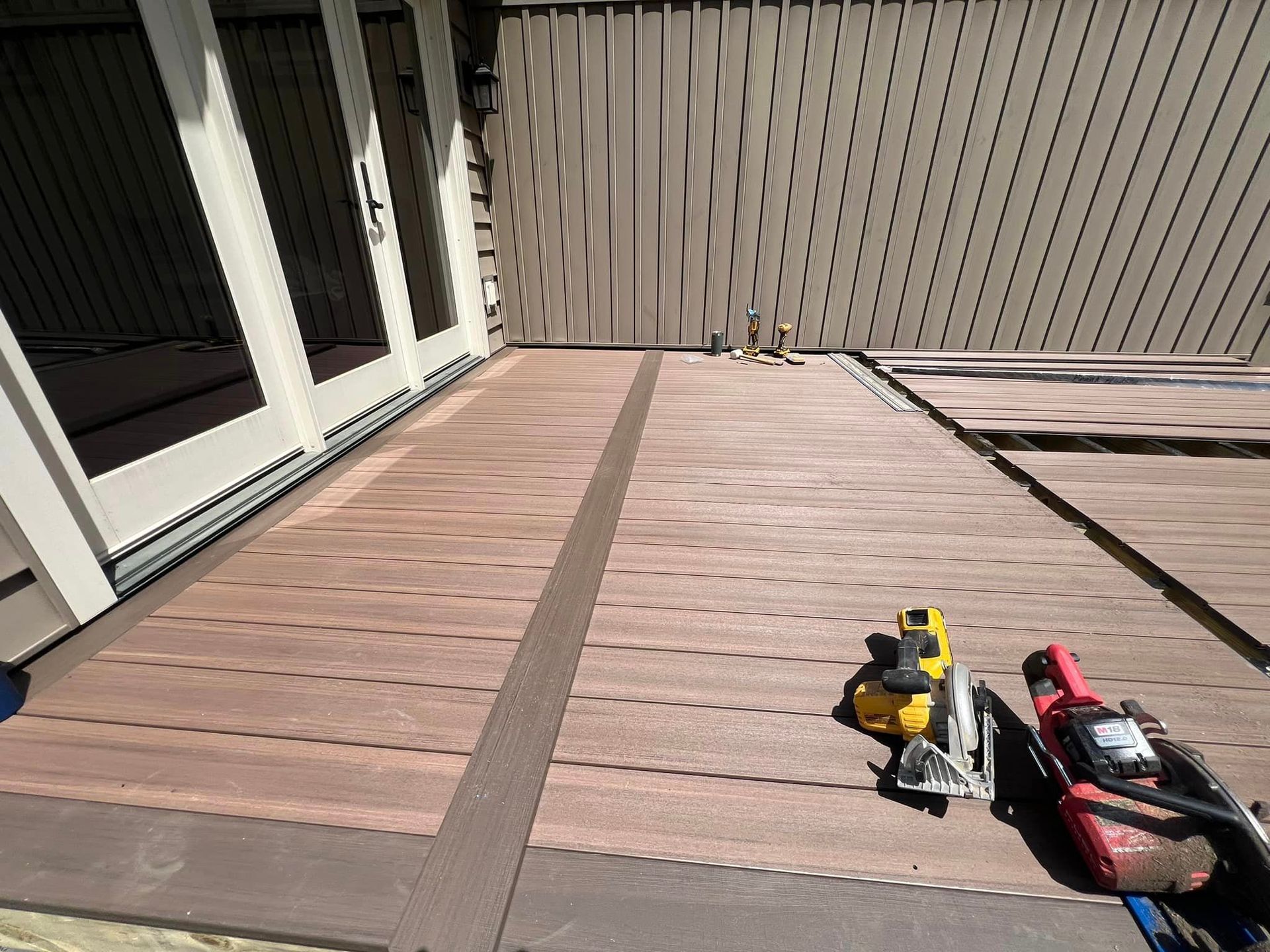 Composite deck boards being installed on a patio, with a circular saw and drill resting on the unfinished surface.