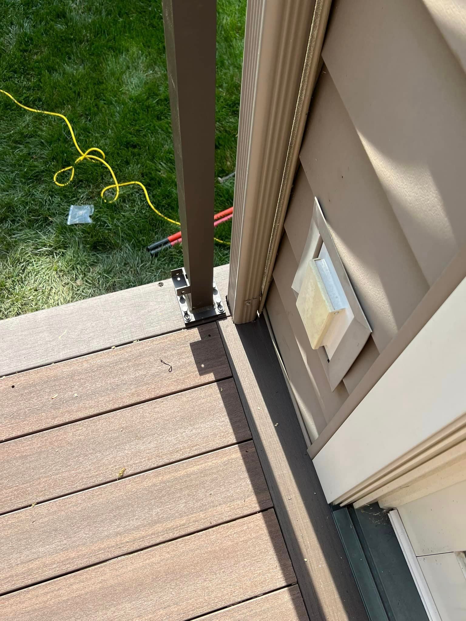 An outdoor deck with brown composite planks, a railing post, and a beige exterior wall vent.