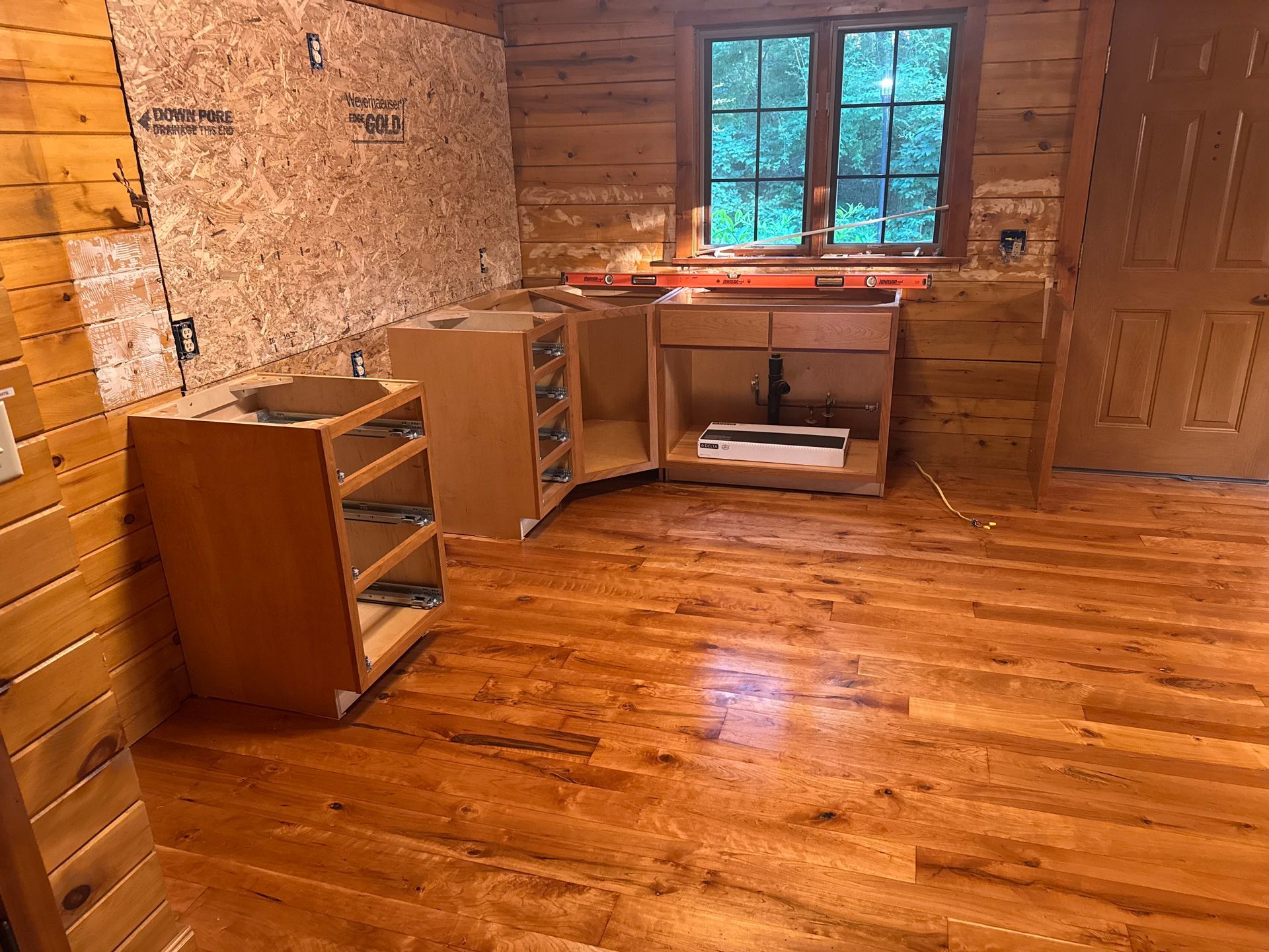 An unfinished kitchen in a log cabin with exposed wood walls, a level on the countertop, and wood flooring.