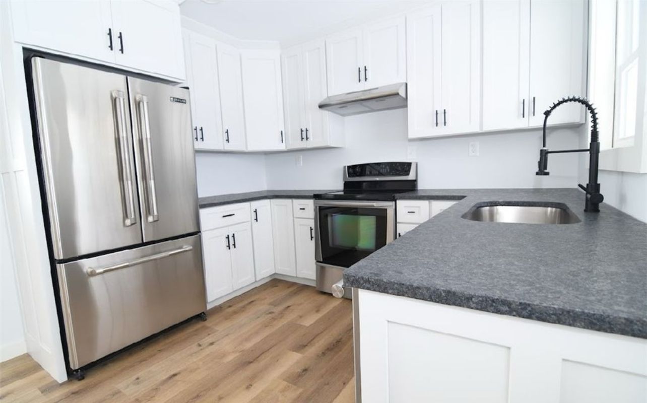 A kitchen with white cabinets, stainless steel appliances, grey countertops, and light-colored wood-look flooring.