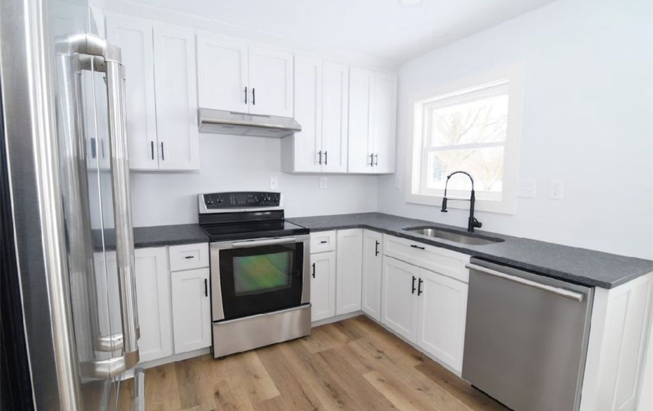 Modern kitchen with white cabinets, dark countertops, stainless steel appliances, and wood-look flooring.