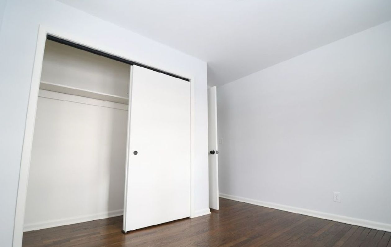 A partially open white closet door in a room with light grey walls and dark hardwood floors.
