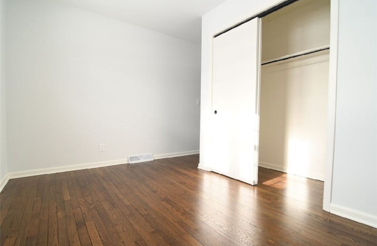 An empty room with light gray walls and dark hardwood floors, featuring an open closet with a white sliding door.