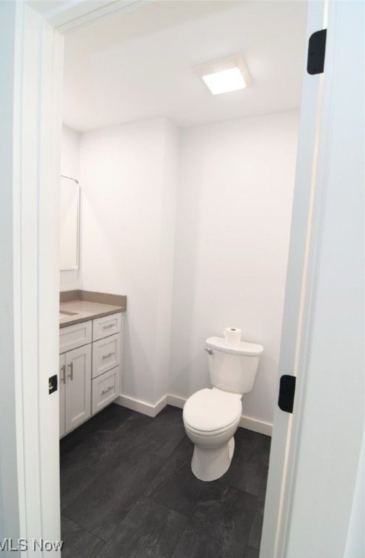 A modern bathroom with white walls, white cabinetry, a white toilet, and dark grey flooring.