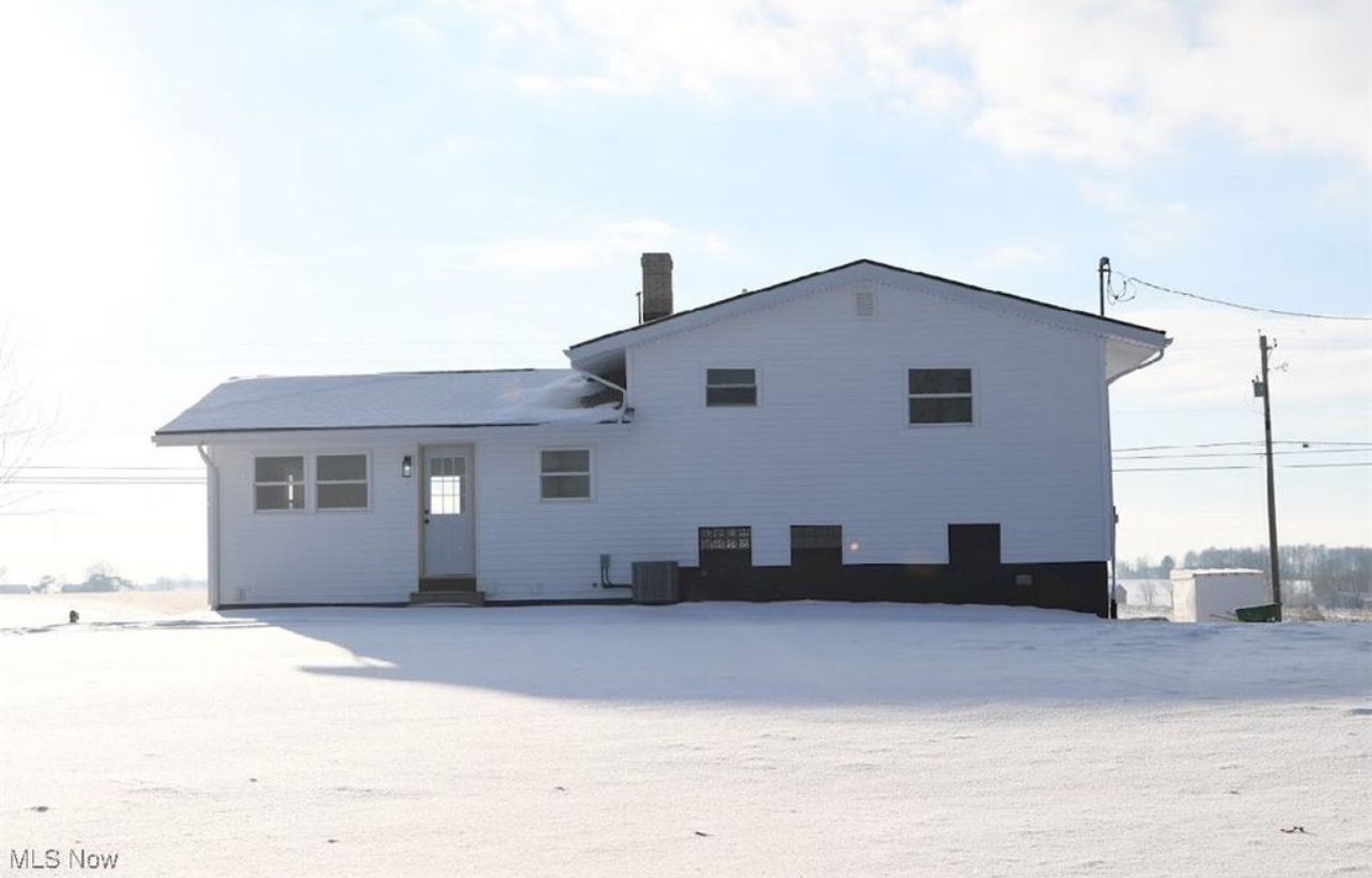 A white split-level house with a chimney and dark foundation set against a snowy landscape under a bright, clear sky.