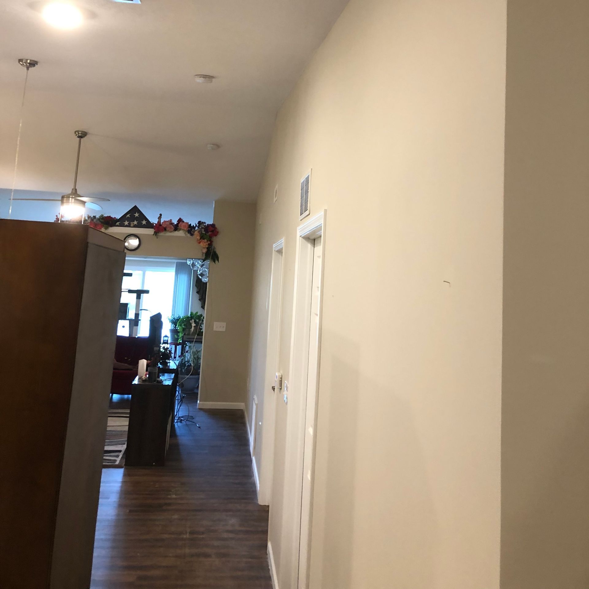 A view down a hallway with beige walls and white door frames, leading toward a brightly lit living area.