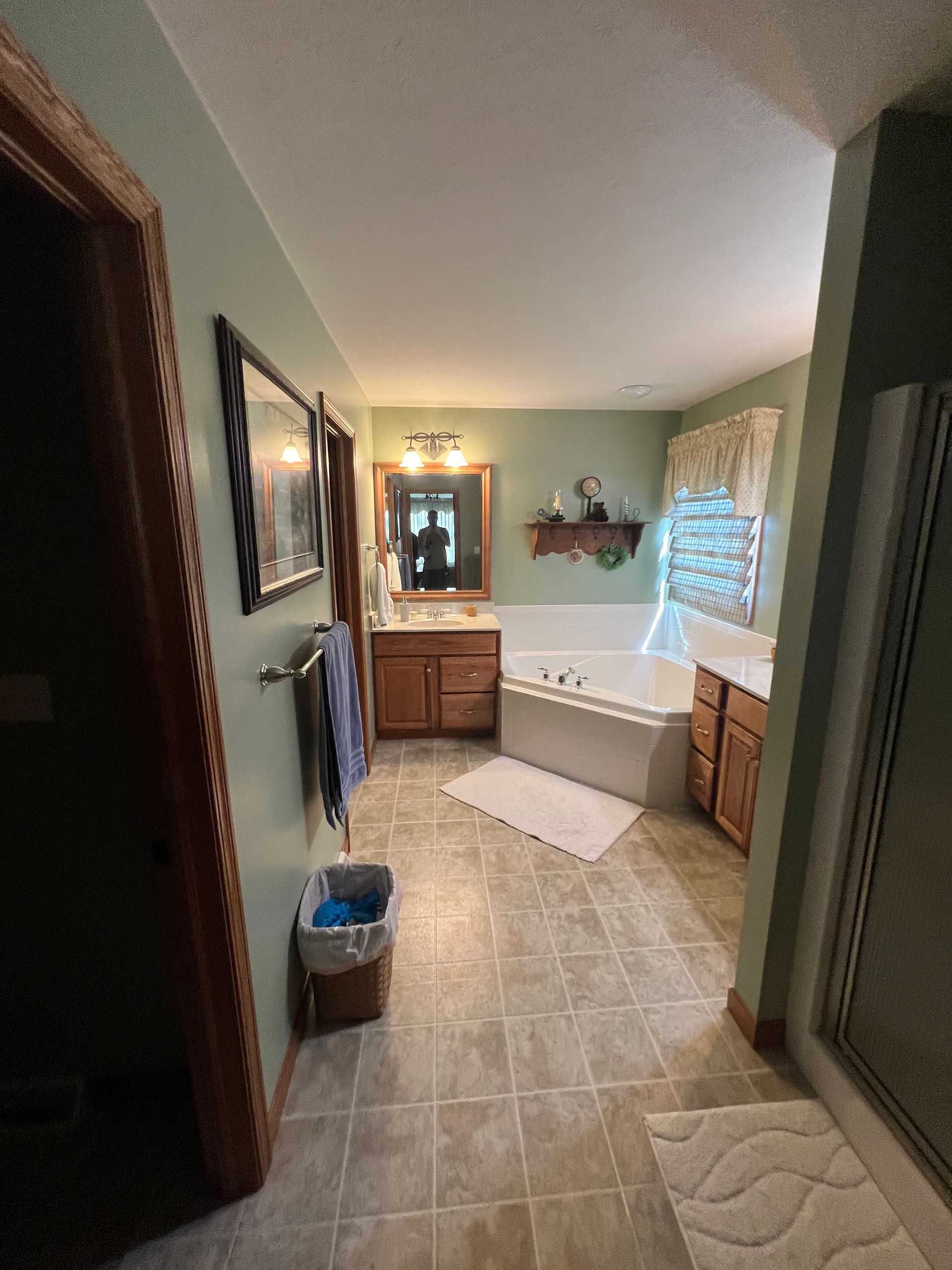 A bathroom with sage green walls, a corner jetted tub, wooden vanity, and tiled floors.