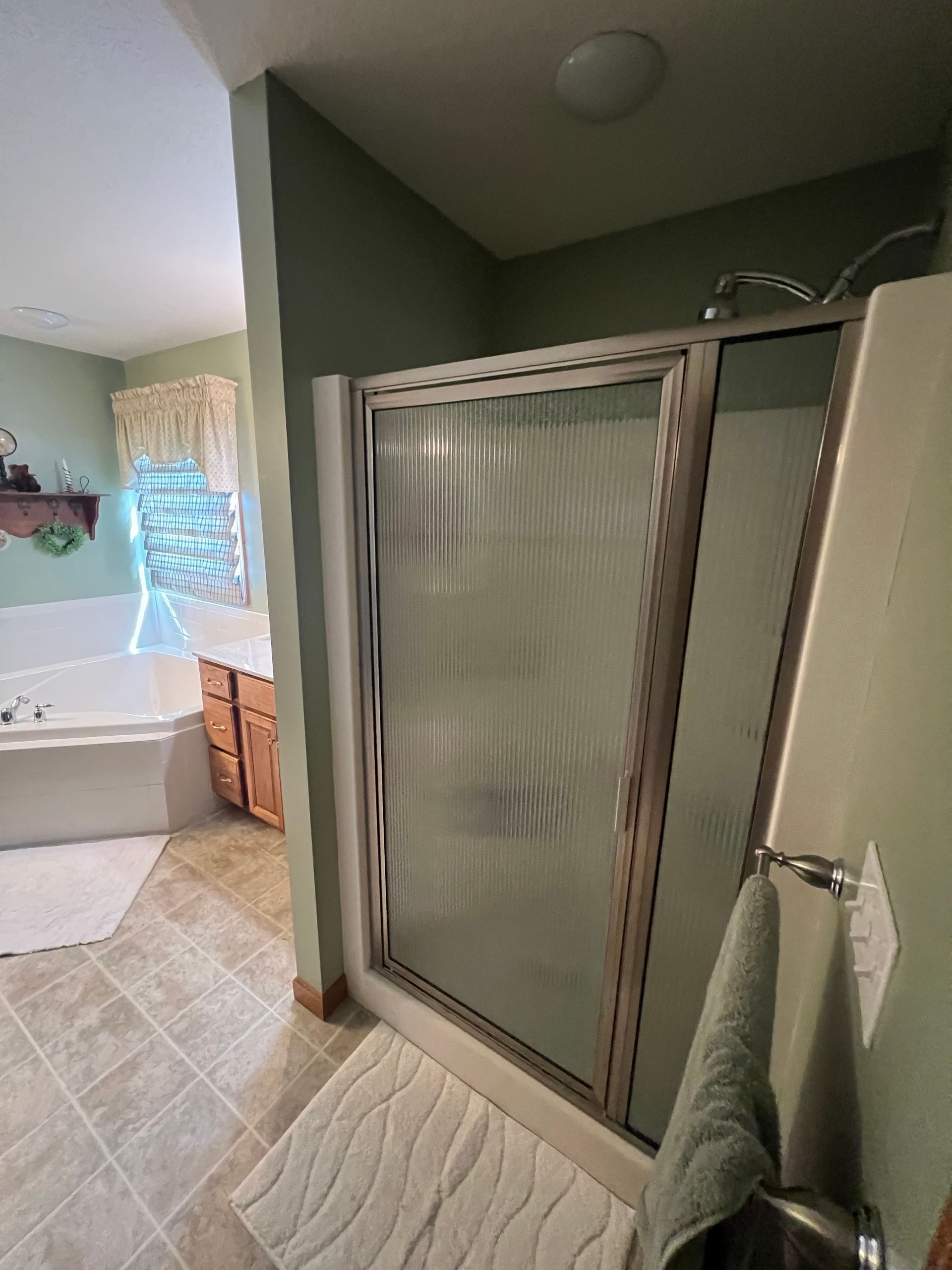 A bathroom with light green walls, a tiled shower stall with glass doors, and a corner bathtub with a wooden vanity.