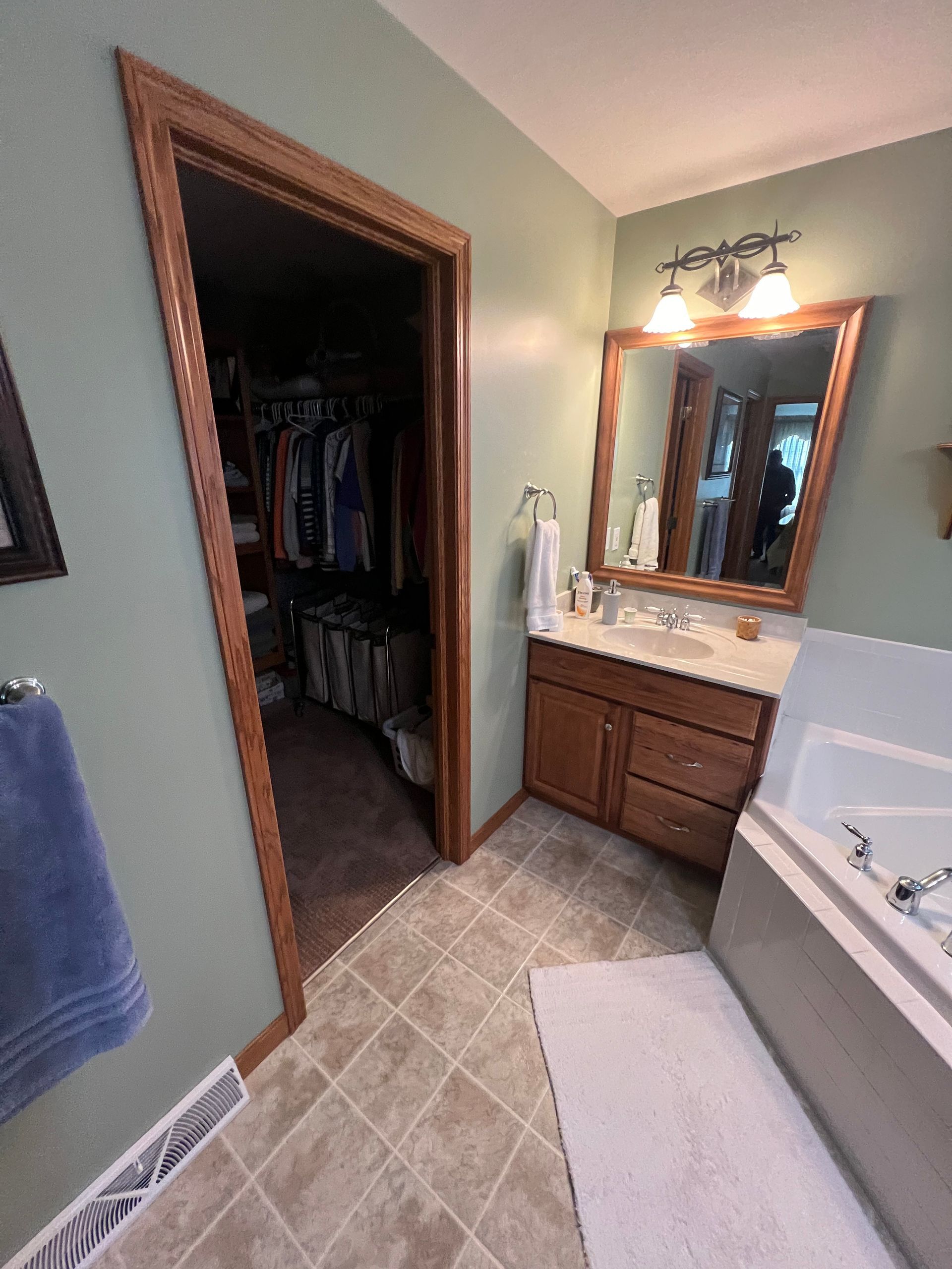 A bathroom with sage green walls, a wood-framed mirror over a wood vanity, a walk-in closet, and a white soaking tub.