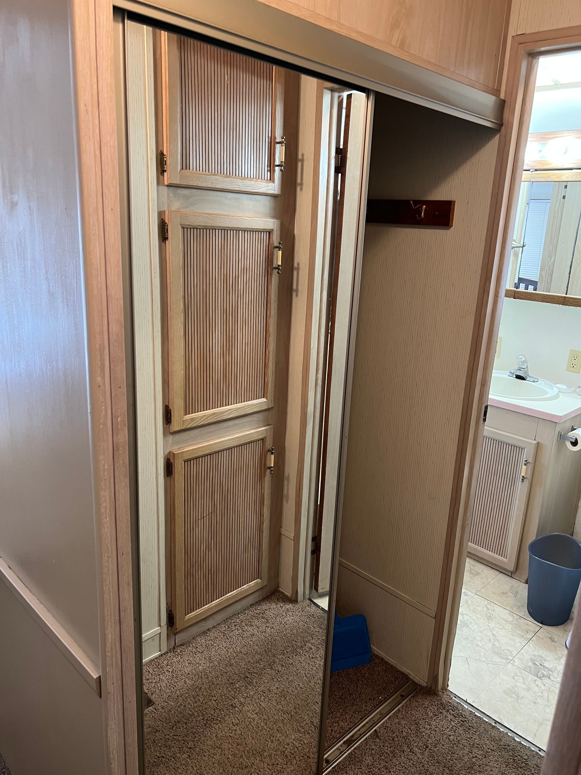 A closet with sliding mirrored doors showing a wood-paneled interior, leading to a bathroom with a sink and vanity.